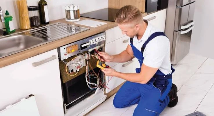Technician testing an exposed kitchen appliance control panel with a multimeter